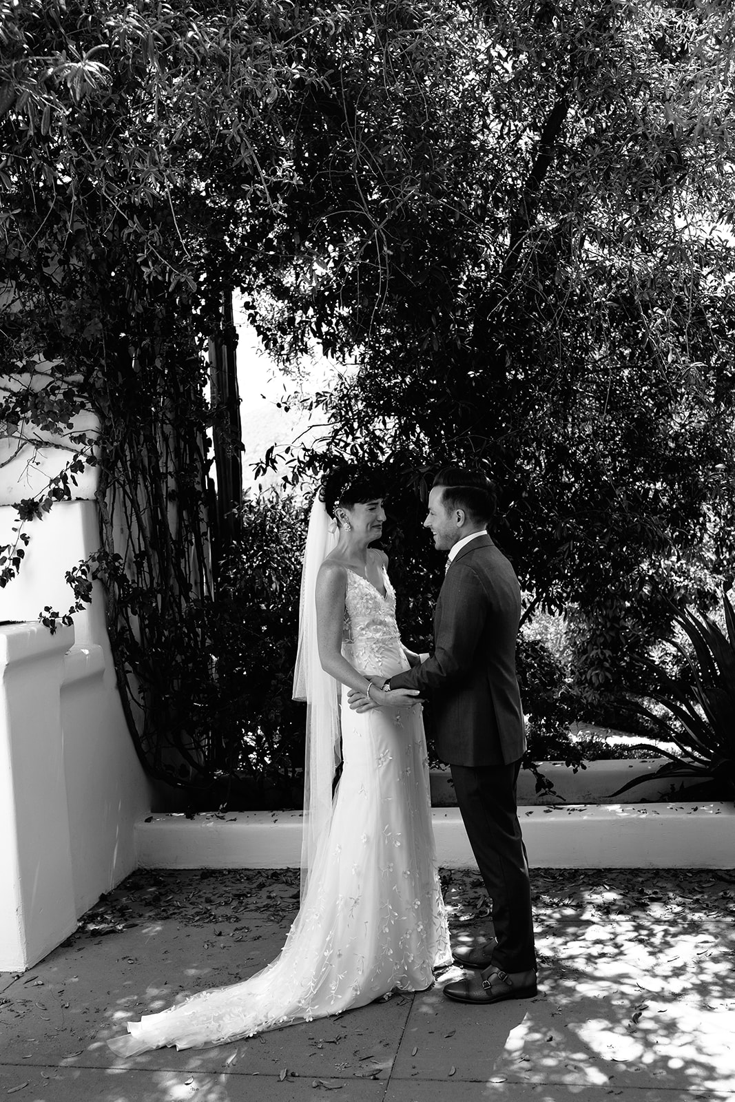 A black and white photo of a bride and groom standing apart, outdoors, with the groom looking at the bride as she walks away as they have their first look at their garden party wedding