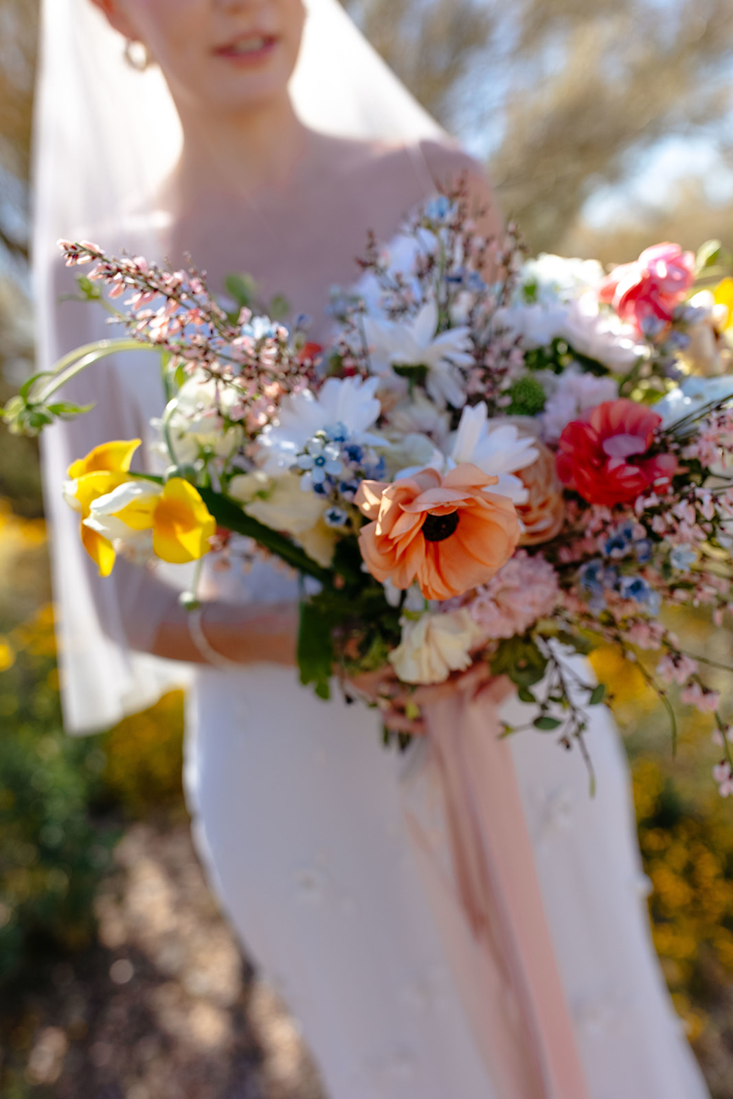 A bride holding a colorful bouquet of flowers, focusing on the bouquet with the bride softly blurred in the background.