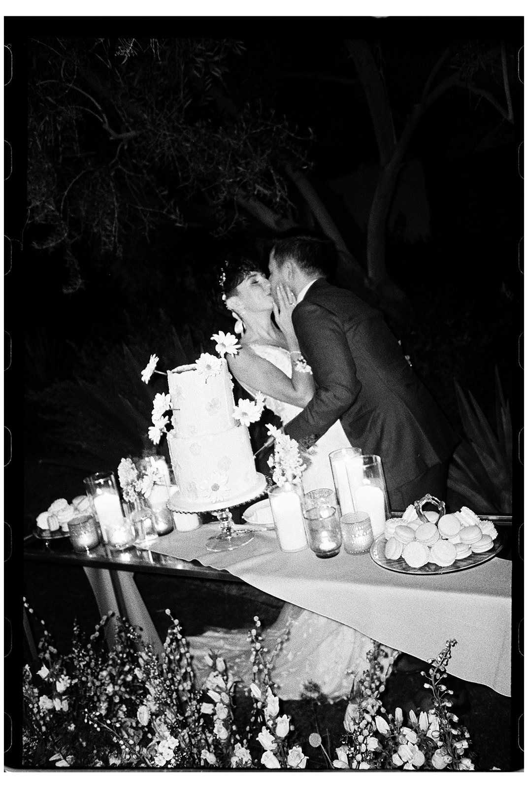 A bride and groom playfully feeding each other cake at their wedding reception, surrounded by candles and decorations.