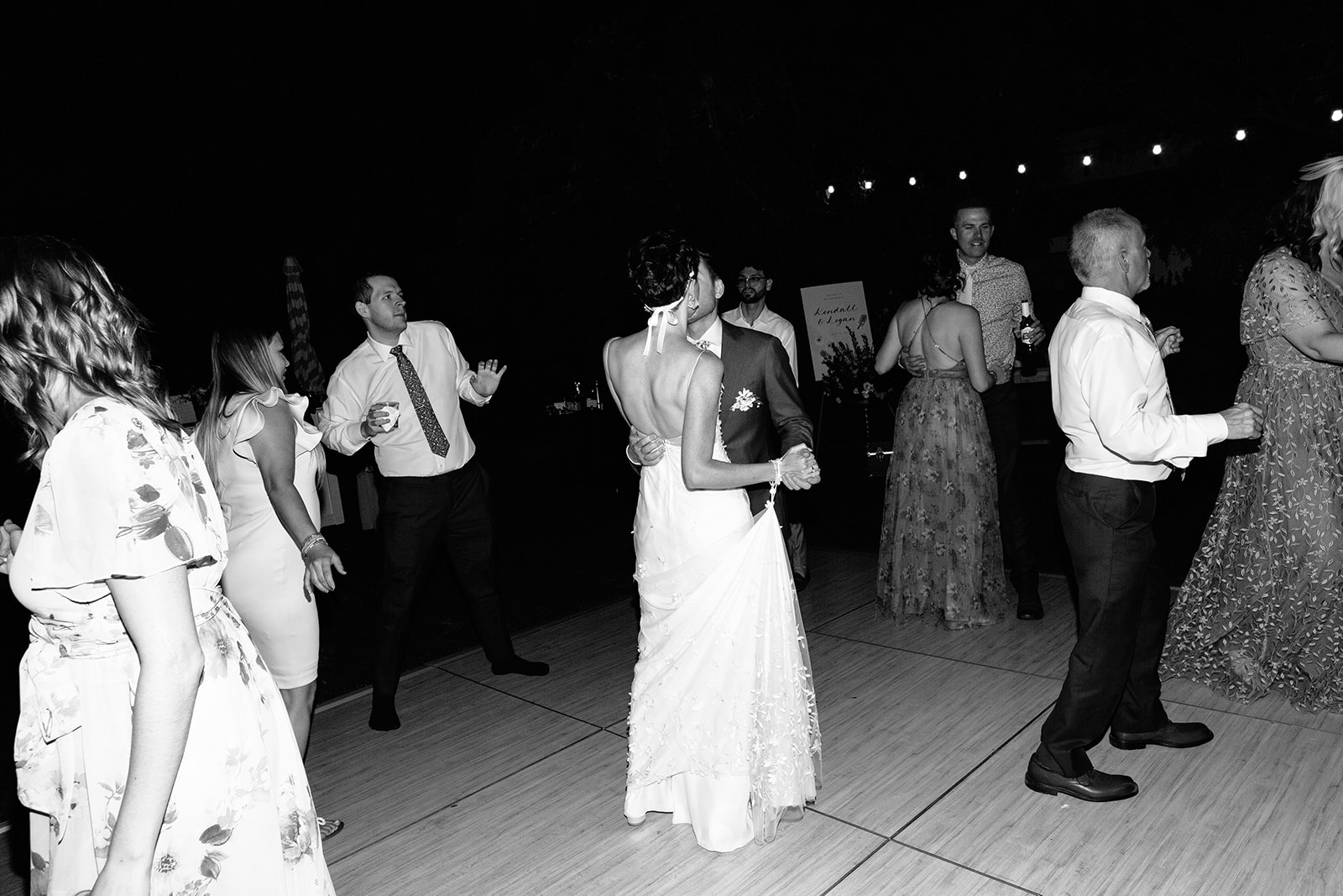 Two women in dresses dance joyfully at a nighttime outdoor wedding reception, surrounded by other guests.