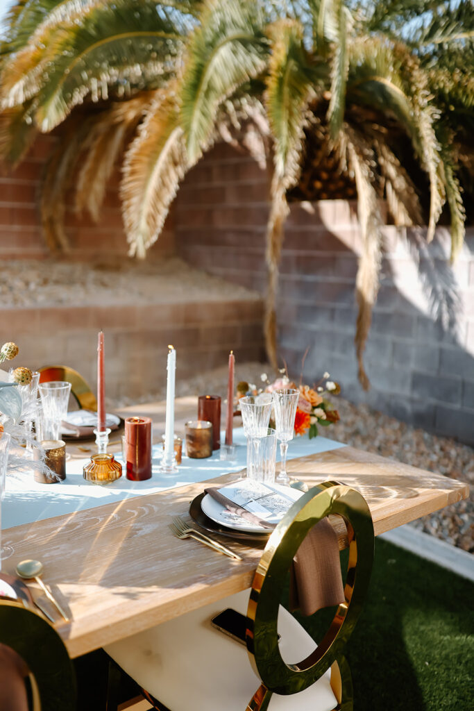 Thanksgiving tablescape setting with a floral arrangement, gold cutlery, crystal glasses, and a brown napkin with a menu on a white plate. Long candles and flower decorations are also in view.