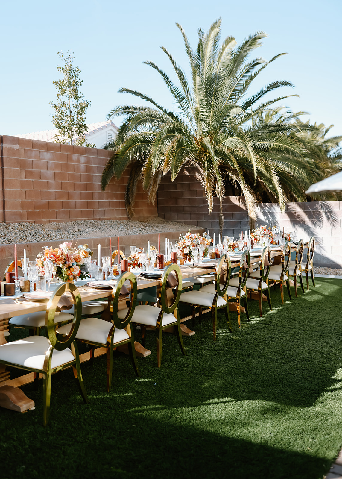 Thanksgiving tablescape setting with a floral arrangement, gold cutlery, crystal glasses, and a brown napkin with a menu on a white plate. Long candles and flower decorations are also in view.