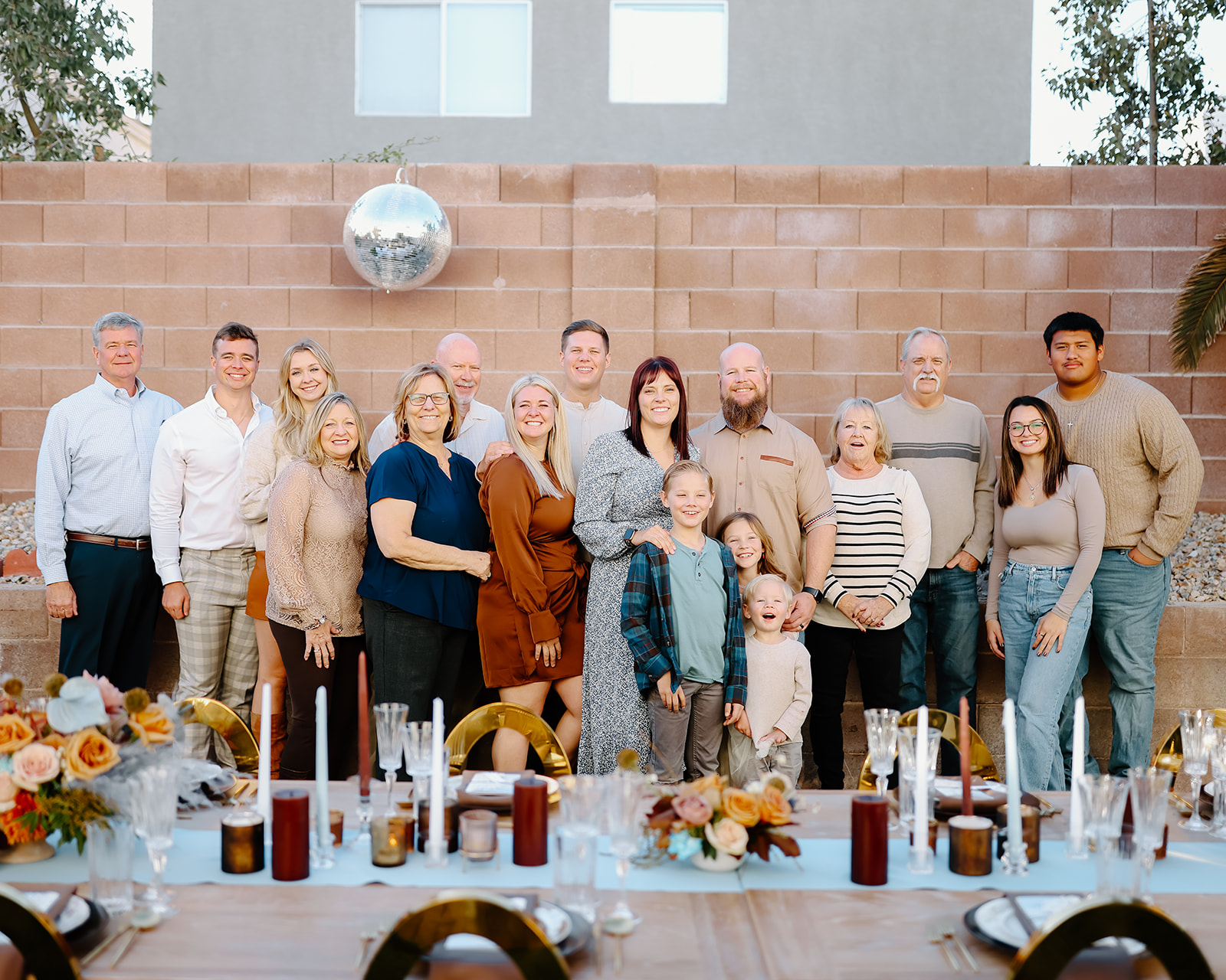 A group of five people standing on grass in an outdoor setting with a palm tree and brick wall in the background for Thanksgiving dinner