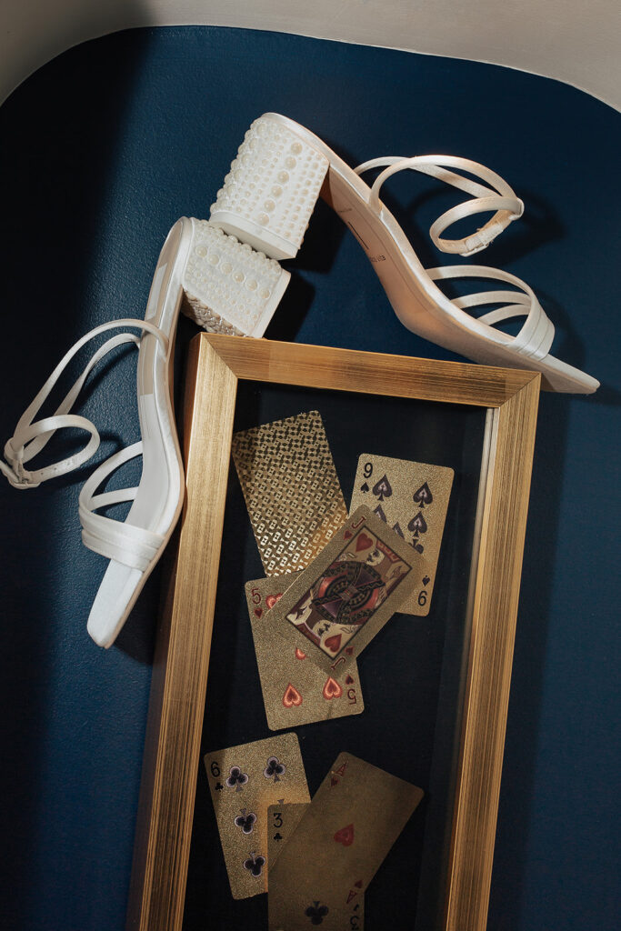 vintage playing cards in shadow box and brides white heels lay on navy blue velvet couch