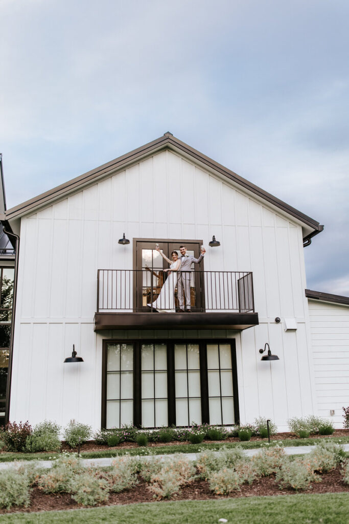 Newlyweds cheers on balcony on side of modern white barn | Timeless