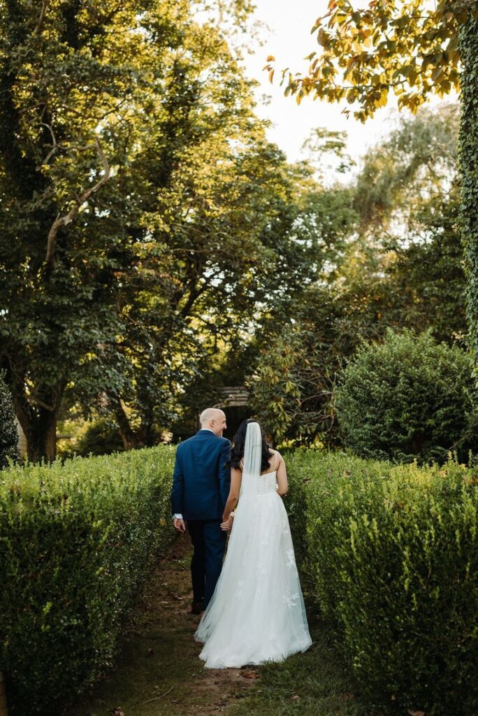 Bride and groom walk through well kept garden of bushes and trees