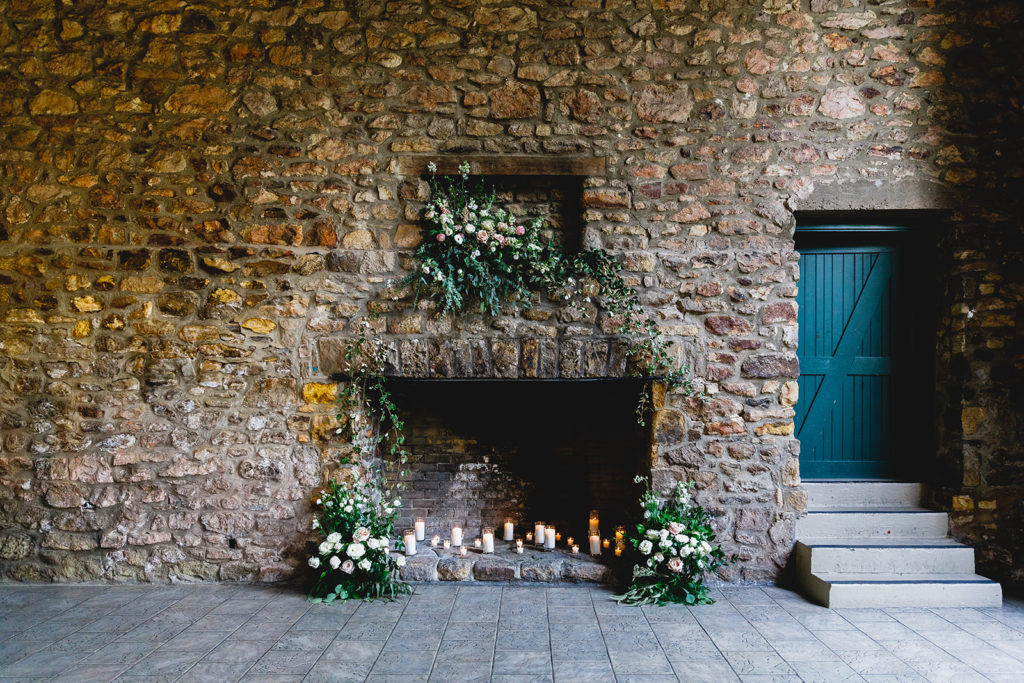 Brick wall and fireplace lined with candles and pink and white floral arrangements | Timeless
