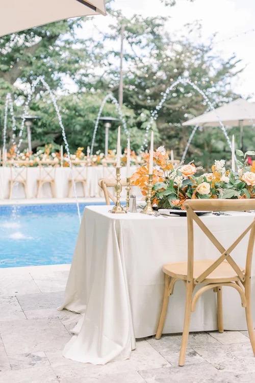 Orange and white tablescapes for reception set up surrounding pool and fountain